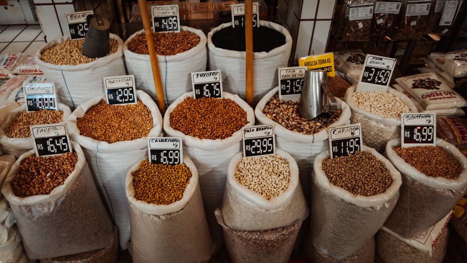 Exposição colorida de mercado com vários feijões em grandes sacos com etiquetas de preço.